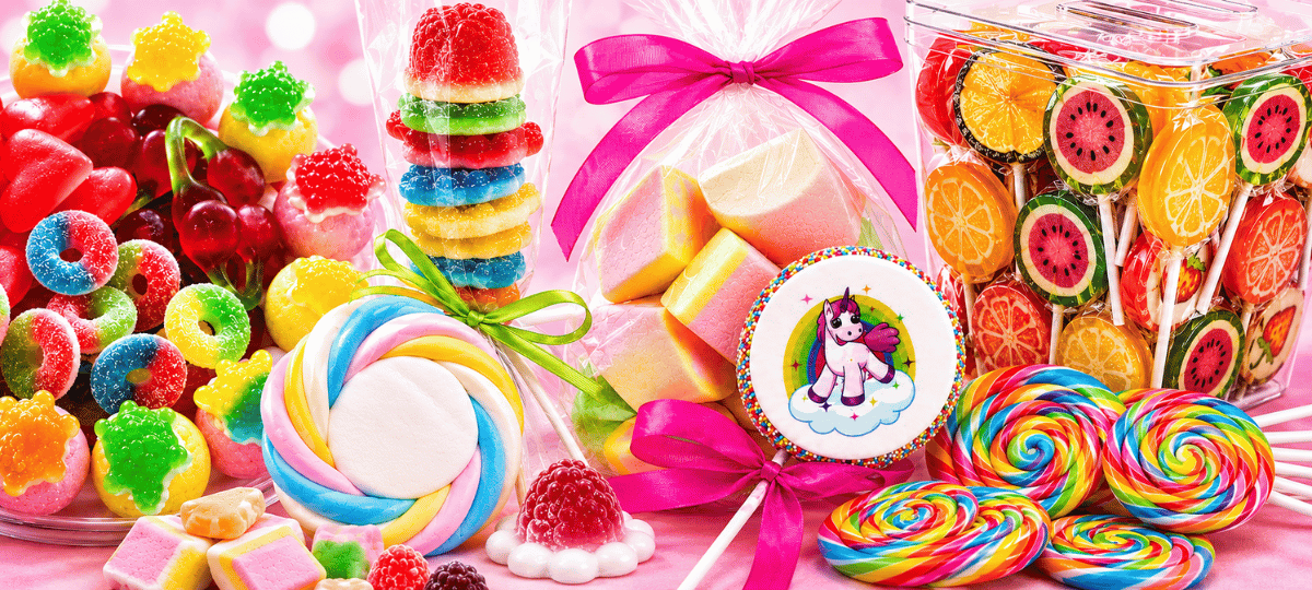 Buntes Sortiment aus Süssigkeiten mit Lollis, Fruchtgummi, Marshmallows und Candy-Spiessen auf rosa Hintergrund – ideal für die Kategorie Candy & Süssigkeiten.